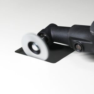 Close-up of a power sander with a spinning circular sanding disk contacting a black square sheet of material at an angle.