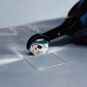 Person using an angle grinder to cut a blue tile on the floor, with protective guard visible and tile outline nearby (informative)
