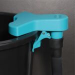 Close-up of a turquoise plastic lid latch and lever attached to the top of a black trash can wiring.