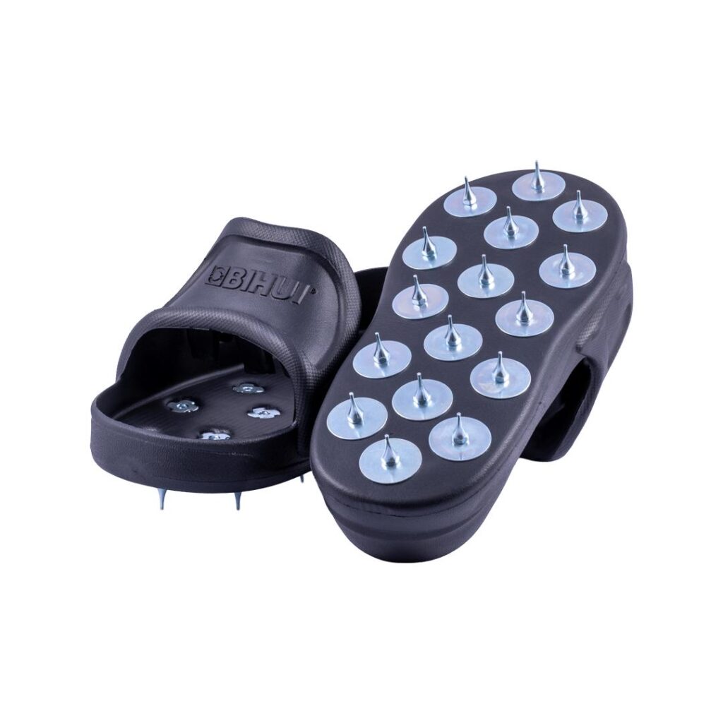 Pair of black acupressure sandals with metal studs on the footbed for massage, viewed from above/side angle.