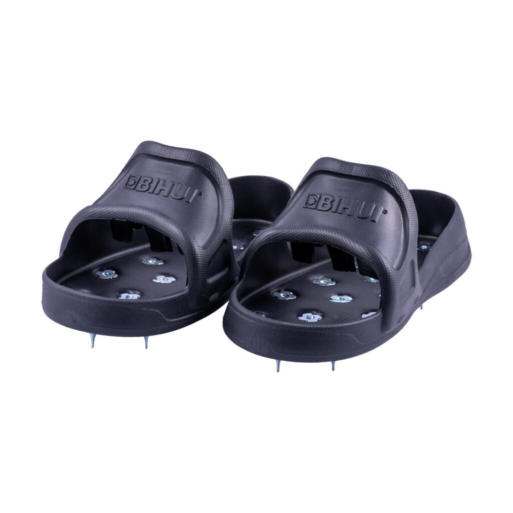 Pair of black slide sandals with metal spikes on the soles for traction.