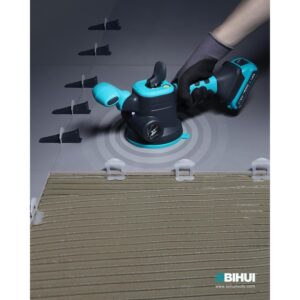 Handheld wireless orbital sander in teal and black sanding a tiled floor, powered by a blue 20V battery.