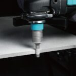 Close-up of a power drill cutting into a metal sheet, with a blue chuck and spiraled shavings visible.