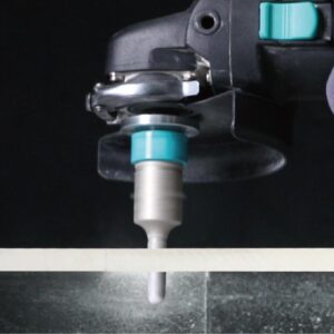 Close-up of a machining drill with teal collet holding a metal rod against a dark background.